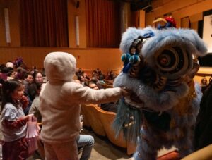 a blue lion greets a small child in fuzzy hooded jacket